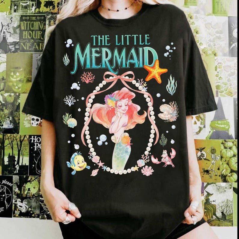 以下が含まれることがあります： 黒いTシャツ。映画「リトル・マーメイド」のアリエルのカラフルなイラストが特徴です。「The Little Mermaid」の文字がターコイズと白で描かれ、ヒトデ、真珠、その他の海の生き物が描かれています。カジュアルでオーバーサイズのフィット感です。