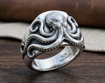 May include: A silver ring featuring a detailed, raised octopus design with textured tentacles wrapping around the band. The interior of the band is clearly engraved with the text 925 HANDMADE, indicating the material composition and production method.