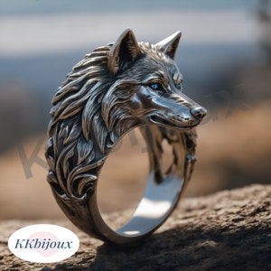 Könnte beinhalten: Ein silberner Ring mit einem detaillierten Wolfskopf-Design. Die Augen des Wolfes sind blau und der Ring liegt auf einer Holzoberfläche.
