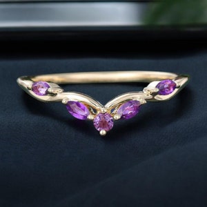 Może przedstawiać: Złoty pierścionek z wzorem w kształcie litery V i pięcioma fioletowymi kamieniami szlachetnymi.