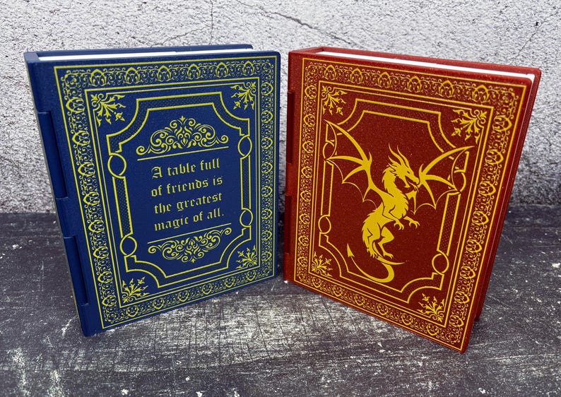 May include: Two decorative books with ornate covers. One is navy blue with gold accents and the quote, "A table full of friends is the greatest magic of all." The other is burgundy with a gold dragon design.