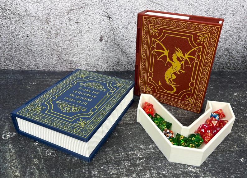 May include: A blue and gold book-shaped box with the quote "A table full of friends is the greatest magic of all." A red book-shaped box with a gold dragon design. A white dice tray holds various colored dice.