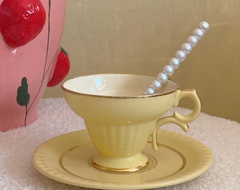 Könnte beinhalten: Ein gelbes Teetassen- und Untertassen-Set mit goldenen Verzierungen. Die Tasse hat ein geriffeltes Design und einen zarten Henkel. Ein perlmuttartiger Löffel liegt auf dem Rand der Tasse.