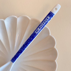 May include: A white ceramic spoon with a blue and white design. The spoon has the words "St. Dalfour" printed on it.