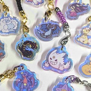 May include: A collection of iridescent acrylic charms featuring various cartoon characters. Each charm is attached to a colorful braided cord with a gold-colored clasp. The charms have a blue outline and are in various shapes.