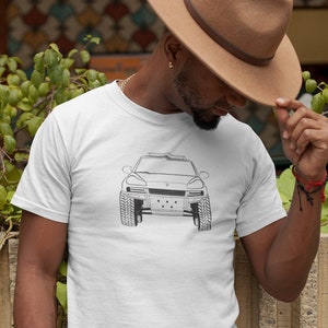 Könnte beinhalten: Ein weißes T-Shirt mit einer schwarzen Linienzeichnung eines Autos auf der Vorderseite. Das Auto hat einen schwarzen Kühlergrill und Scheinwerfer. Die Person, die das Shirt trägt, trägt einen braunen Hut.