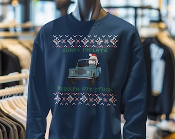 May include: Navy blue sweatshirt with a festive design. The text "SORRY I'M LATE" and "RUDOLPH GOT STUCK" are displayed above and below a cartoon image of a vehicle with a reindeer wearing a Santa hat. The design includes snowflakes.