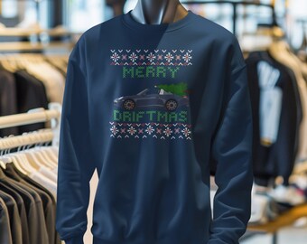 May include: Navy blue sweatshirt with a festive design. The design includes the text "MERRY DRIFTMAS" in green, a car, and snowflake patterns. The sweatshirt is displayed on a mannequin.