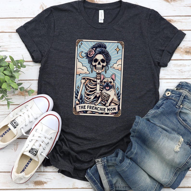 May include: Dark gray t-shirt featuring a tarot card design with a skeleton, a French Bulldog, and the text "THE FRENCHIE MOM." The shirt is paired with white sneakers and blue jeans.