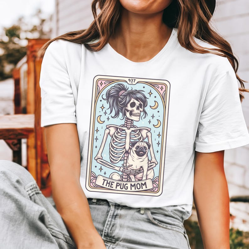 Puede incluir: Camiseta blanca con un gr&aacute;fico de una mujer esqueleto sosteniendo un pug. El gr&aacute;fico est&aacute; en estilo de carta de tarot con el texto "The Pug Mom" en la parte inferior.