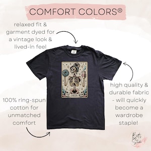Pode incluir: Uma camiseta azul escura com uma ilustra&ccedil;&atilde;o vintage de um esqueleto segurando uma x&iacute;cara de caf&eacute; e um pompom. O texto "The Cheer Mom" est&aacute; impresso abaixo do esqueleto. A camiseta &eacute; feita de 100% algod&atilde;o ring-spun e tem um caimento relaxado.
