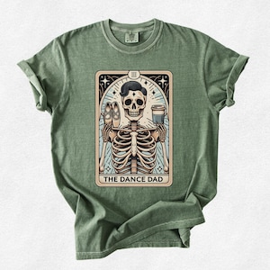 May include: Green t-shirt with a vintage tarot card design featuring a skeleton holding a coffee cup and ballet shoes. The card reads "The Dance Dad" and has the Roman numeral III at the top.