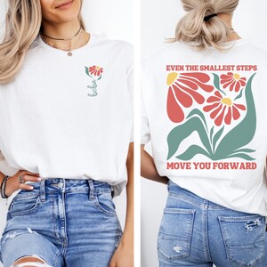May include: White t-shirt with a floral design and the text "Even the smallest steps move you forward" on the back. The front of the shirt has a small flower design and the word "bloom" written vertically.