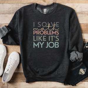May include: A dark gray sweatshirt with the text "I solve math problems like it's my job" in colorful letters.