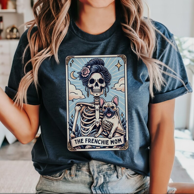May include: Dark blue t-shirt featuring a tarot card design with a skeleton, a French Bulldog, and the text "THE FRENCHIE MOM". The card has a light blue background with clouds, a crescent moon, and stars.