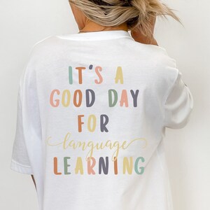 May include: White t-shirt with the text "It's a good day for language learning" in colorful letters.