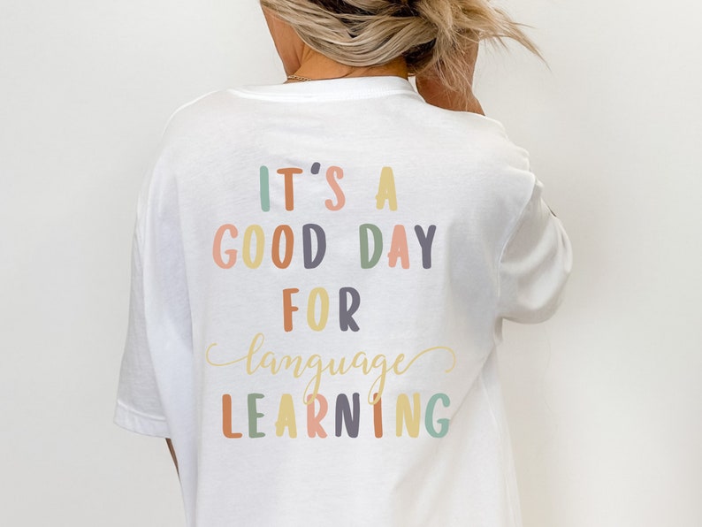 May include: White t-shirt with the text "It's a good day for language learning" in colorful letters.