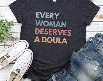 May include: A dark heather grey t-shirt with the text "EVERY WOMAN DESERVES A DOULA" printed in rainbow colours.