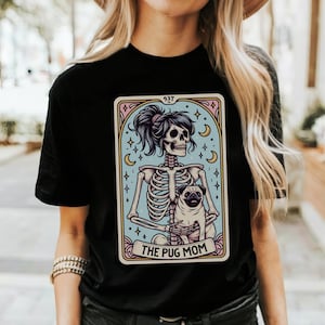 Puede incluir: Camiseta negra con un gr&aacute;fico de una mujer esqueleto sosteniendo un pug. El gr&aacute;fico est&aacute; en estilo de carta de tarot con el texto "The Pug Mom" en la parte inferior.