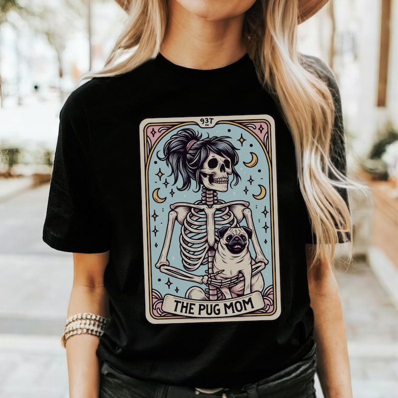 Puede incluir: Camiseta negra con un gr&aacute;fico de una mujer esqueleto sosteniendo un pug. El gr&aacute;fico est&aacute; en estilo de carta de tarot con el texto "The Pug Mom" en la parte inferior.