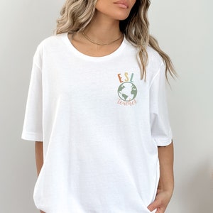 May include: White t-shirt with a graphic of a globe and the text "ESL teacher" in colorful letters.