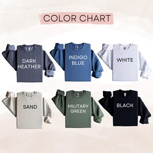 May include: A color chart displaying six long-sleeve crewneck sweatshirts in dark heather, indigo blue, white, sand, military green, and black. Each sweatshirt features its corresponding color name printed in bold black or white text on the front.