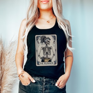 May include: Black tank top featuring a tarot card design with a skeleton figure. The card reads "THE RUNNER" in a decorative frame. The skeleton has a headband and is holding a small bag. The tank top is worn by a person.