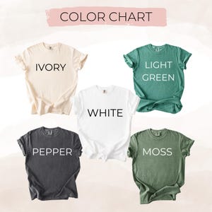 May include: A color chart displays five t-shirts in various colors: ivory, white, light green, pepper, and moss. Each shirt has its color name printed in a bold, sans-serif font. The shirts are neatly arranged against a soft, neutral background.