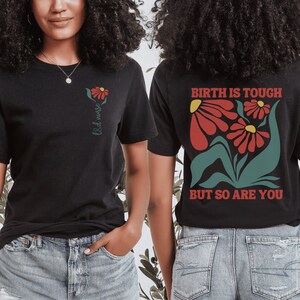 May include: Two black t-shirts with different designs. The first shirt has a single red flower with green leaves and the text "L&D nurse". The second shirt has a floral design with red flowers and green leaves and the text "Birth is tough but so are you".