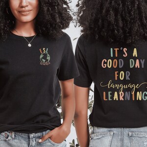 May include: Black t-shirt with the text "ESL teacher" and a globe graphic on the front. The back of the shirt has the text "It's a good day for language learning" in colorful letters.