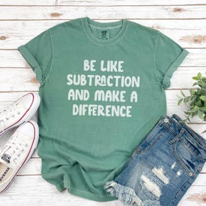 May include: A green t-shirt with the text "Be like subtraction and make a difference" in white.