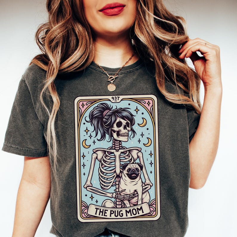 Puede incluir: Una camiseta gris oscuro con un gr&aacute;fico de un esqueleto sosteniendo un pug. El gr&aacute;fico est&aacute; en un estilo de carta de tarot con el texto "The Pug Mom" en la parte inferior.