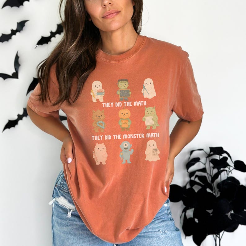 May include: A burnt orange t-shirt featuring a graphic of cartoon monsters with the text "THEY DID THE MATH" and "THEY DID THE MONSTER MATH". The shirt is a short-sleeved, crew neck style.