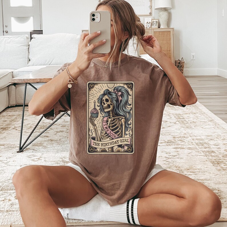 May include: A brown t-shirt featuring a graphic of a skeleton holding a cupcake and a sash that reads "It's My 30th The Birthday Girl".