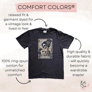 May include: Dark navy blue t-shirt with a graphic featuring a skeleton woman with a husky dog, the text "THE HUSKY MOM", and the words "COMFORT COLORS". The shirt is made of 100% ring-spun cotton.