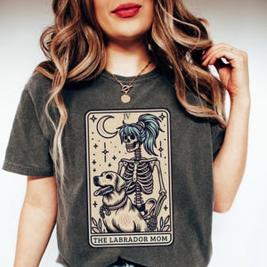 May include: A dark gray t-shirt with a tarot card design featuring a skeleton holding a dog. The card reads "The Labrador Mom" and "IV".