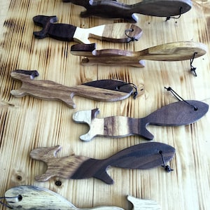 May include: A collection of wooden squirrel-shaped bottle stoppers in various shades of brown and tan. Each stopper has a black cord attached for easy removal. The wooden stoppers are arranged on a light brown wooden surface.