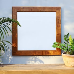 May include: A brown wooden framed mirror with a white background. The mirror is hanging on a light blue wall. There is a green plant in a terracotta pot on a wooden table in front of the mirror.
