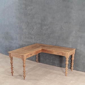Könnte beinhalten: Ein hellbrauner, L-förmiger Holzschreibtisch mit zwei kleinen Schubladen und verzierten, gedrechselten Beinen. Der Schreibtisch ist aus Massivholz gefertigt und hat eine natürliche Oberfläche. Der Schreibtisch ist ca. 152 cm lang.