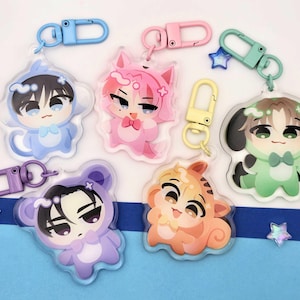 May include: Five acrylic keychains featuring cartoon characters in animal costumes. The characters are colored blue, pink, green, purple, and orange, each with a matching plastic lobster clasp. The designs include a cat, dog, and bear motif.