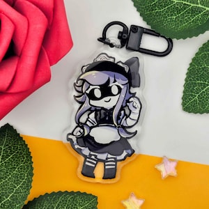May include: A clear acrylic keychain featuring a cartoon character in a maid outfit with purple hair and a black bow. The keychain has a black clasp and is set against a yellow and white background with a red rose and green leaves.