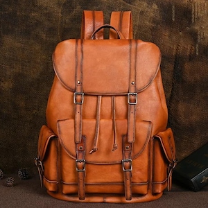 Könnte beinhalten: Ein brauner Lederrucksack mit Klappenverschluss, zwei Vordertaschen und verstellbaren Trägern. Der Rucksack hat Metallschnallen und einen oberen Griff. Die Tasche ist etwa 40 cm hoch, 30 cm breit und 15 cm tief.