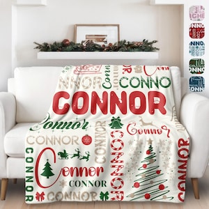 May include: White fleece throw blanket with a Christmas theme. The blanket features the name "Connor" repeated in red, green, and gold lettering, along with Christmas trees, candy canes, and snowflakes.