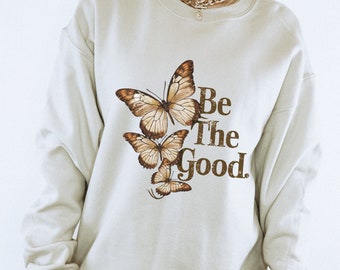 May include: A light beige sweatshirt with a brown butterfly graphic and the text "Be The Good."