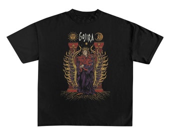 May include: Black t-shirt featuring a graphic of a robed figure with a crown, holding a snake, and surrounded by flames. The word "GOJIRA" is above the figure, with sun and moon symbols on either side. The design is in shades of red, purple, and gold.