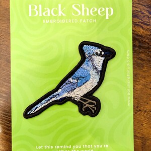 May include: An embroidered patch of a blue jay bird with blue, white, and black thread, mounted on a lime green card. The card features the text Black Sheep EMBROIDERED PATCH and Let this remind you that you're a gift to the world.