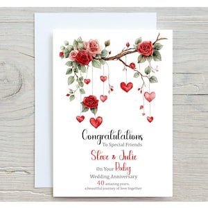 May include: A white anniversary card with a floral design. The card features red roses, hanging hearts, and the words "Congratulations", "Steve & Julie", and "On Your Ruby Wedding Anniversary".