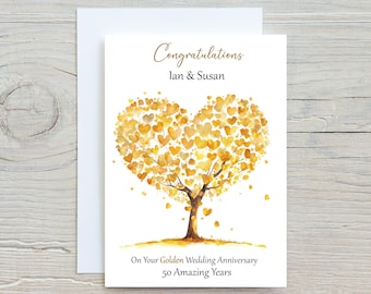 May include: A white greeting card with a watercolor illustration of a tree with a heart-shaped crown made of golden hearts. The card reads "Congratulations Ian & Susan" and "On Your Golden Wedding Anniversary 50 Amazing Years."