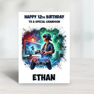May include: A birthday card with a blue, green and white design featuring a young person playing a video game. The card says "Happy 12th Birthday to a Special Grandson" and "Ethan".