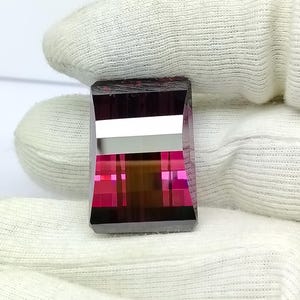 Pode incluir: Uma gema retangular de cor rosa escura e marrom com um corte facetado.